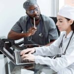 Two medical professionals entering data submissions on a laptop