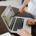 Two people pointing at dynamic drop-down menu on laptop