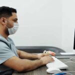Man wearing face mask while entering data using computer keyboard